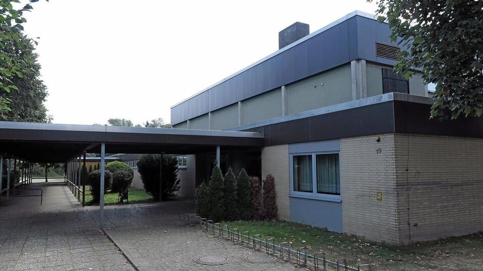 Moderner, einst&ouml;ckiger Bau mit Flachdach und gro&szlig;en Fenstern, umgeben von Gr&uuml;nanlagen und Gehwegen.