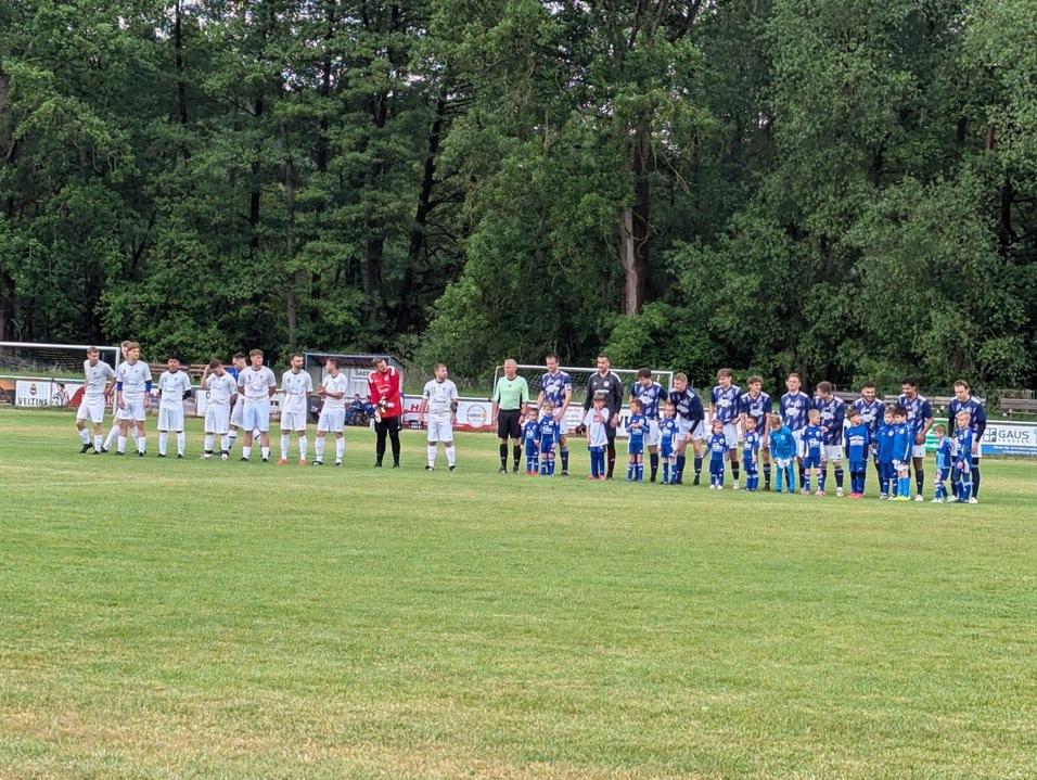 Zwei Fu&szlig;ballmannschaften in wei&szlig;en und blauen Trikots stehen auf einem Rasenplatz, um sich auf das Spiel vorzubereiten.