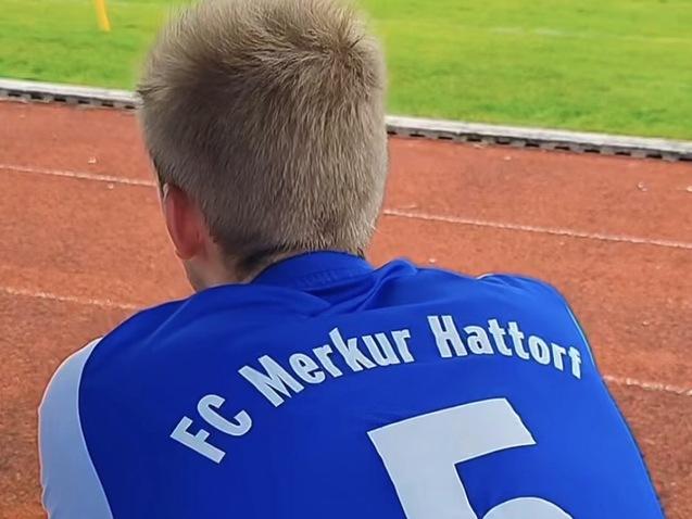 Junger Mann von hinten in einem blauen Fu&szlig;balltrikot mit der Aufschrift &bdquo;FC Merkur Hattorf&ldquo; und der Nummer 5.