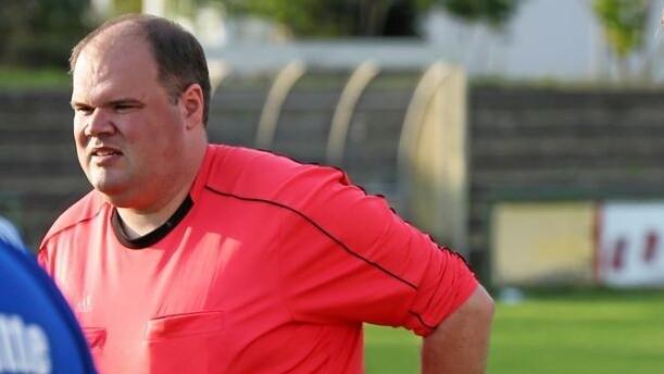 Drei Schiedsrichter in roten Trikots stehen auf einem Fußballfeld und besprechen sich.